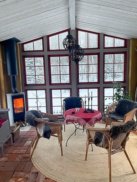 Uterum med stora spröjsade fönster, runt matbord och rottingfåtöljer mot snötäckt utsikt.