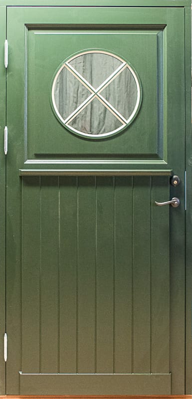 Grön ytterdörr med runt glasfönster med krysspröjs och stående panel nedtill.