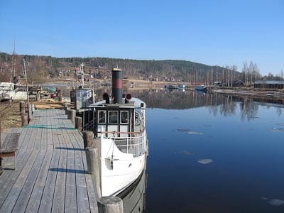 Vit båt förtöjd vid en lång träbrygga vid stilla vatten en klar dag