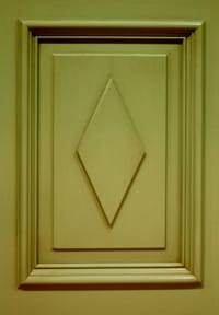 Detaljbild av profilerad dörrspegel i mjukt grönbeige ton med upphöjd diamantformad dekorruta centrerad i mitten.