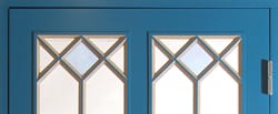 Detaljbild av blå dörr med två dekorativa glasöppningar, spröjsade i kryss- och diamantmönster med ljust frostat glas bakom.