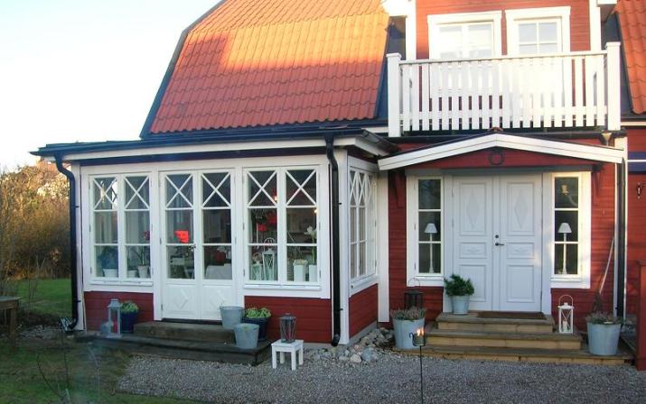 Rött trähus med vita detaljer, veranda med stora fönster med spröjs och en vit pardörr med speglar och rombformade dekorationer.
