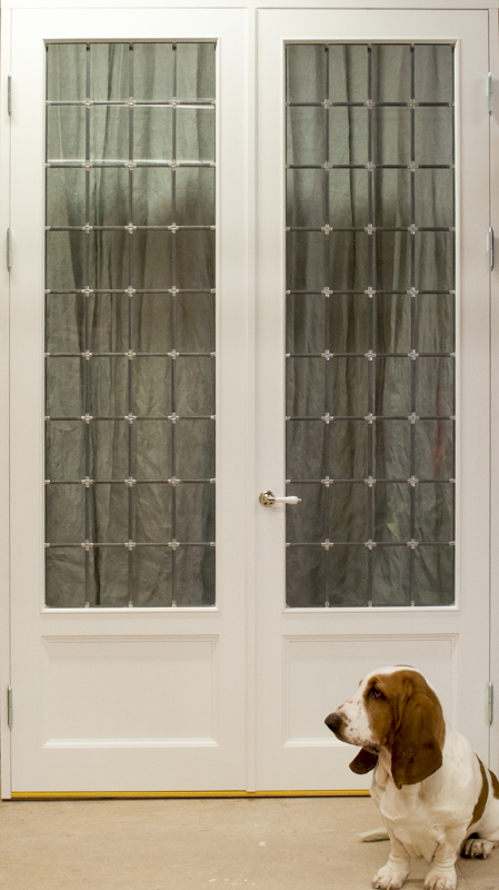 Vit pardörr med glasrutor i rutmönster och träspeglar längst ned, framför dörren sitter en hund.