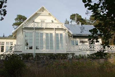 Verandafasad på vit trävilla med höga spröjsade fönsterpartier och glasdörrar samt balkong med vit krysspanel.