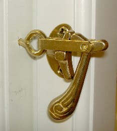 Närbild av klassiskt, mässingsfärgat fönsterbeslag/hasp med svängt dekorativt handtag, monterat på en vit profilerad karm.
