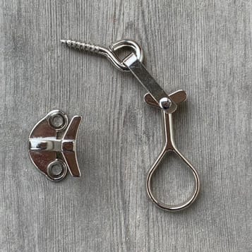 Produktbild av kromad fönsterhasp i två delar: en skruvögla med droppformat handtag och en separat liten metallplatta med två skruvhål som fäste.
