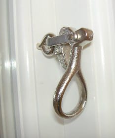 Närbild av blankt droppformat fönsterbeslag/hasp i metall, monterat på en vit profilerad karm.