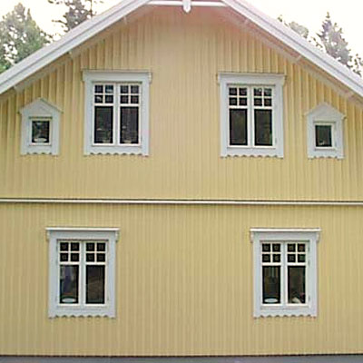 Gult trähus med stående panel och vita foder. Fasaden visar två våningar med symmetriskt placerade fönster. På nedervåningen sitter två större fönster med spröjs i övre delen, och på övervåningen tre större spröjsade fönster samt två små triangulära fönster längst ut på sidorna.