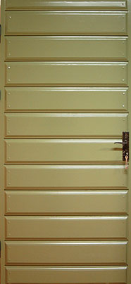 Grön dörr i trä med liggande profilerade panelbrädor. Dörren har en enkel metallhandtag i mörk färg på höger sida och gångjärn på vänster sida.