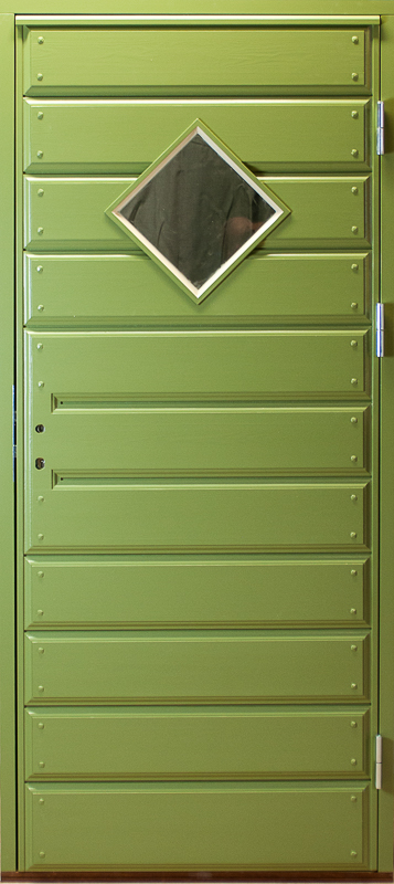 Grön paneldörr med liggande brädor och markerade rader av nitar längs varje panel. I övre delen finns ett diamantformat fönster med vit ram. Dörren har metallgångjärn på höger sida och en enkel, robust design med symmetriska linjer.