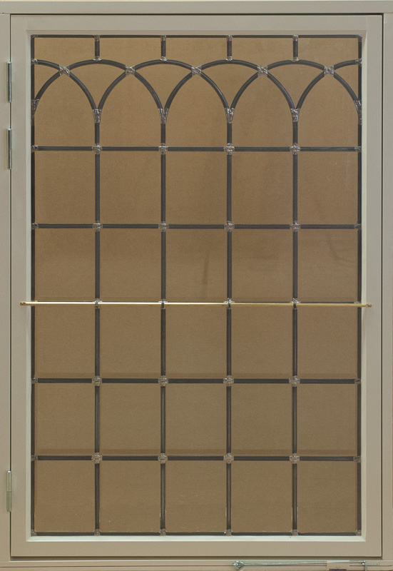 Ett högt sidohängt fönster med beige karm och blyinfattat glas. Glaset är indelat i små rutor med spröjs där den övre delen pryds av fyra spetsbågade mönster i gotisk stil. Resten av glasytan är uppdelad i jämna fyrkantiga rutor, vilket skapar en klassisk och tidlös känsla.