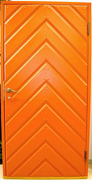 Orange dörr med kraftig diagonal panel i fiskbensmönster. Panelerna bildar ett V-format mönster som sträcker sig från toppen till botten. Handtaget sitter på vänster sida och dörren är förstärkt med små nitar längs panelerna.