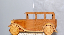 Närbild av träbil i gammaldags stil där högra delen av bilen syns genom maskinantikt glas som gör bakgrunden mjukt suddig.