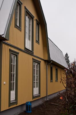 Gul träfasad med flera fönster med enkel spröjs och vit dörr i klassisk stil.