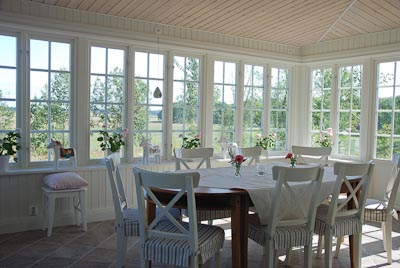 Interiör i glasveranda med många spröjsade fönster i rutnät och matplats.