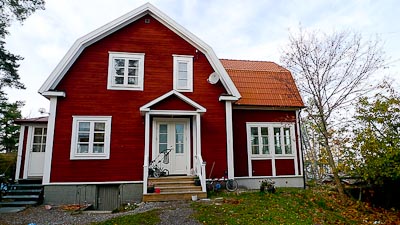 Södersida av rött hus med spröjsade fönster i rutnät och klassiska proportioner.