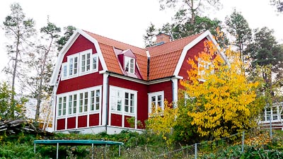 Rött hus med flera spröjsade fönster och verandapartier, vit foderinramning.