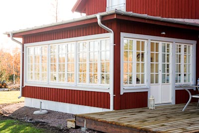 Utsida av veranda/altan med lång rad spröjsade fönster i rutnät och vit dörr.