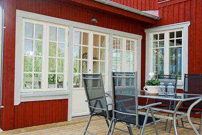 Uteplats vid röd fasad med spröjsade fönster och vit pardörr/fönsterdörr.