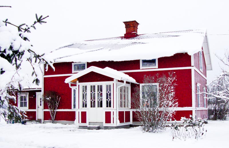 Rött hus i vintermiljö med farstukvist och fönster med dekorativ spröjs.