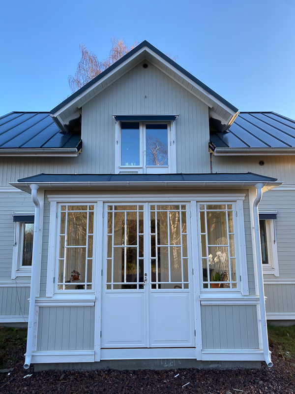 Front av glasveranda med spröjsade fönster och glasade dörrar som släpper in ljus.