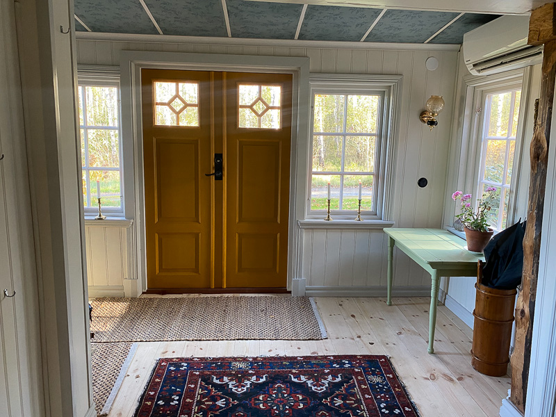 Gul pardörr med diamantformade glasrutor i överdelen, flankeras av sidoljusfönster och spröjsade fönster i ljus karm.