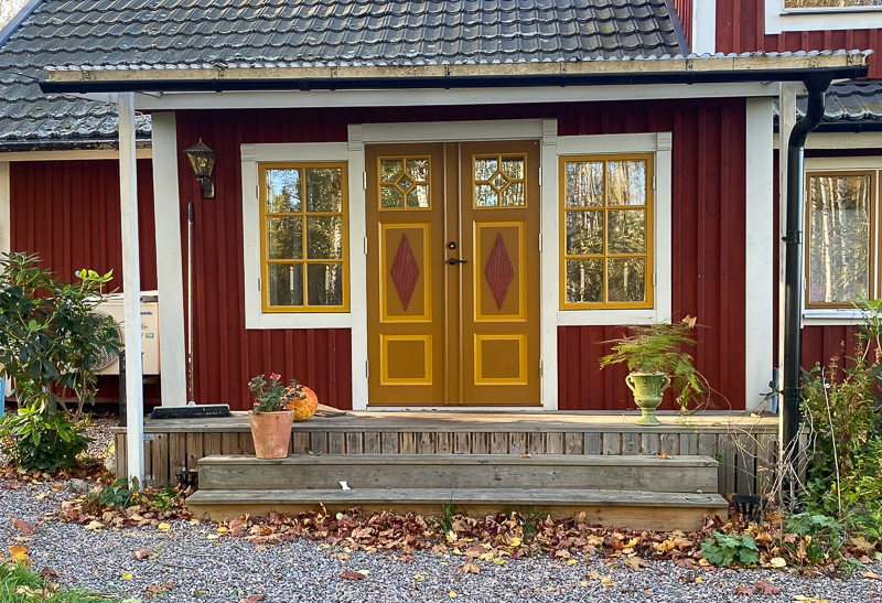 Entré med två fönster i gul karm och glasrutor med dekorativ spröjs, som släpper in ljus till hallen.