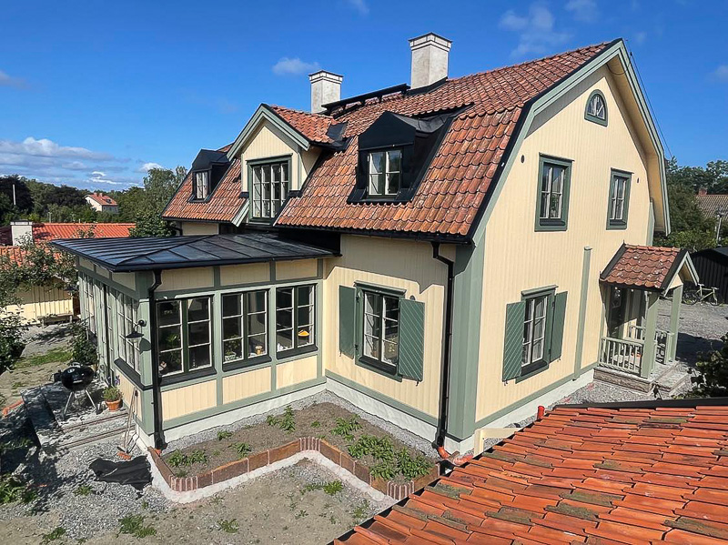 Gavelvy med glasveranda och flera höga fönsterpartier i mörkgrön karm, med stora glasytor och spröjs.