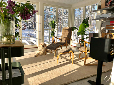 Interiör i glasveranda med spröjsade fönster från golv till tak i vinkel, där vinterlandskapet syns tydligt genom rutorna och ljuset flödar in.