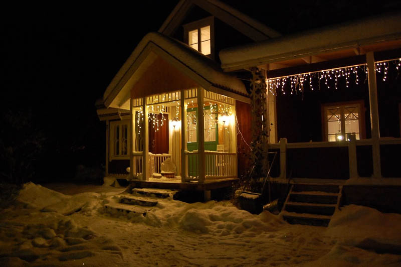 Kvällsbild av hus med farstukvist och spröjsade fönster, detaljer med torpromb och kryss.