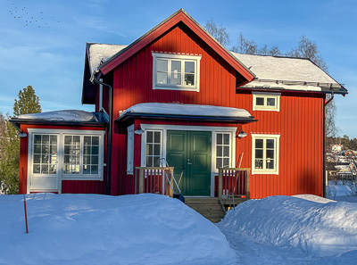 Rött hus i vinterljus med flera vitmålade spröjsade fönster i fasaden, inklusive större fönsterpartier som speglar himlen och förstärker det klassiska uttrycket.