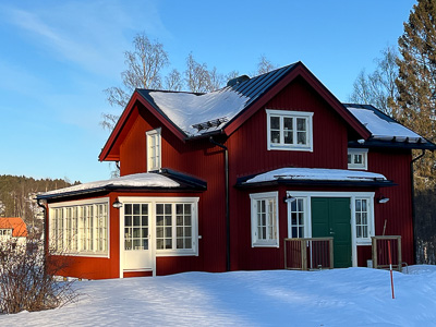 Rött hus efter renovering med vitmålade spröjsade fönster, stort fönsterparti i tillbyggnad samt entré med sidoljus som släpper in mycket dagsljus.