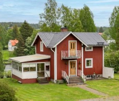 Rött hus före renovering med äldre fönstersättning, inklusive en inglasad/verandaliknande del med fönster i rad samt fönsterdörrar och mindre fasadfönster.