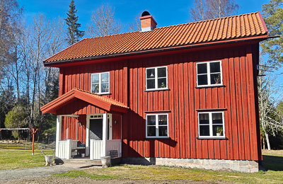 Röd husfasad med flera vita spröjsade fönster i jämn placering över två plan, där fönstren lyfter det klassiska uttrycket mot den ljusa himlen.