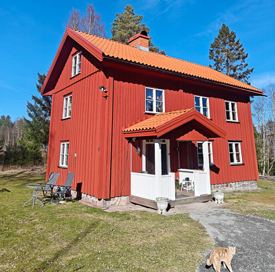 Rött trähus med vita spröjsade fönster på två våningar och glasade partier vid farstukvisten, där fönstren ramar in fasaden och speglar dagsljuset.