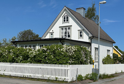 Vit villa med flera spröjsade fönster i olika storlekar, inklusive fönster på övervåning och i gavel, som ger huset ett klassiskt uttryck.