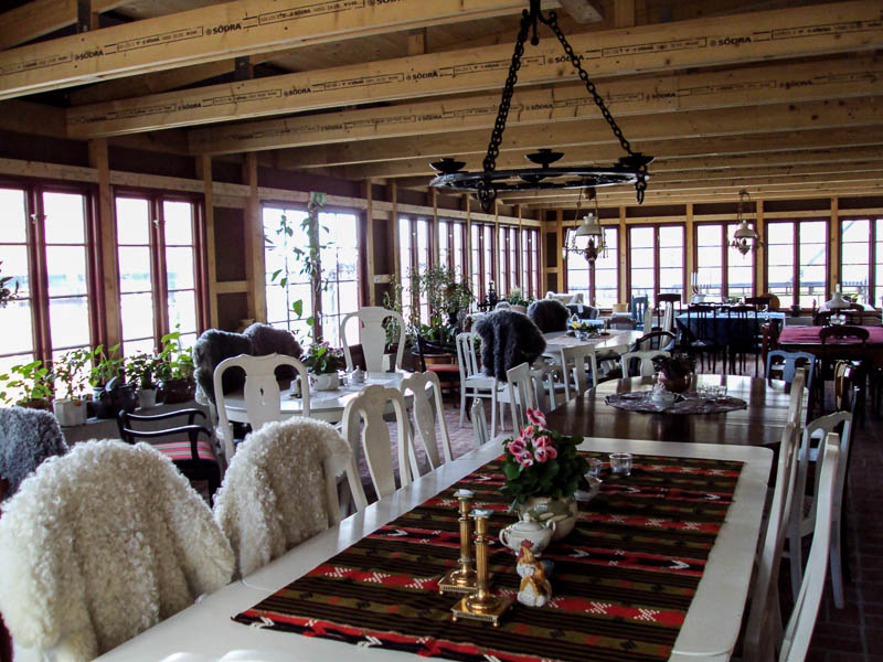 Stort verandarum/café med många spröjsade fönster i rutnät och ljusa möbler.