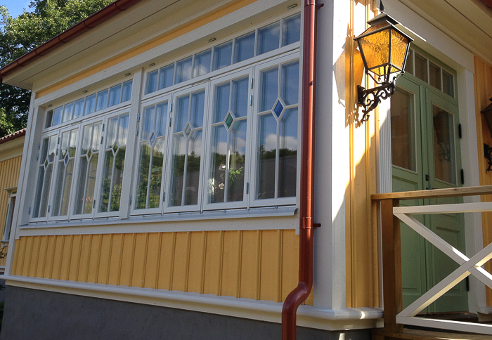 Verandaparti med lång fönsterrad med romb/diamant-detaljer och grön glasad dörr.