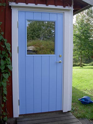 Blå paneldörr med stående panel och rektangulärt glasfält utan spröjs.