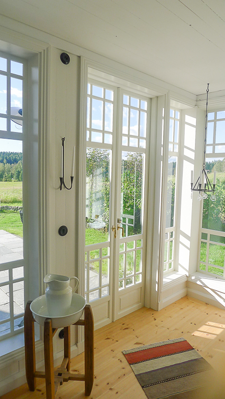 Ljus hörna i glasveranda med spröjsade fönsterpartier och fönsterdörr med spegelkänsla nedtill.