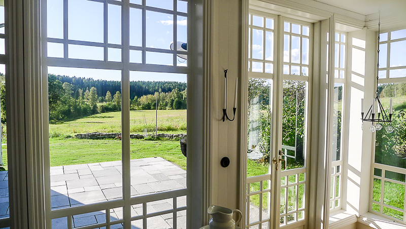 Inifrån glasveranda med spröjsade fönster och fönsterdörr i klassisk stil mot uteplats.
