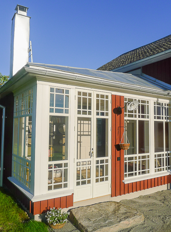 Röd fasad med vit glasveranda, fönster och dörrpartier med spröjs i rutnät.