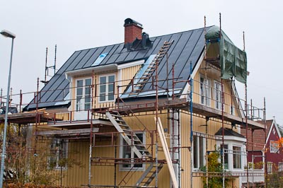 Tvåvåningshus under byggnation med byggställning och nya fönster längs fasaden.