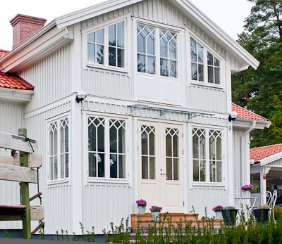 Vit veranda med spröjsade fönster och kryss/diagonal-spröjs i överkant samt pardörr i mitten.