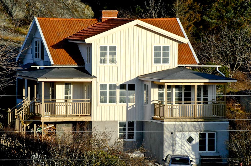 Vitt hus med verandor, spröjsade fönster och en dekorativ rombformad detalj i fasaden.