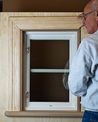 Person som står bredvid ett nyinstallerat fönster med vit karm, infällt i en fönsternisch av ljust trä med färdigmonterad fönsterbänk.