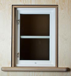 Färdig fönsternisch med vitmålat öppningsbart fönster, omgiven av ljus träpanel och med matchande fönsterbänk nedtill.